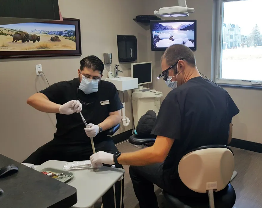 Two clinicians in scrubs and masks working together at a treatment-room chairside.