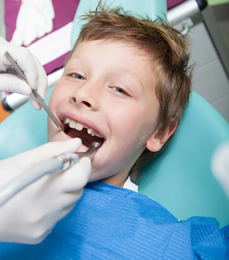 A young boy in a dental chair having his teeth examined with a mirror and probe.