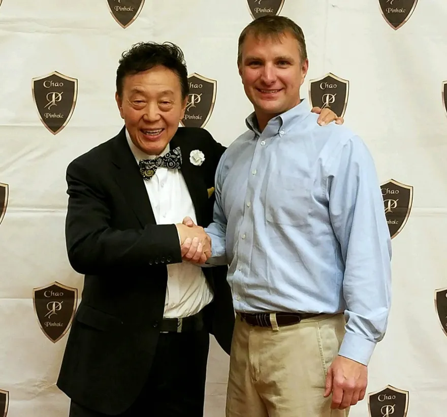 Dr. John Chao and Dr. Scott Beck shaking hands in front of a Chao Pinhole backdrop.
