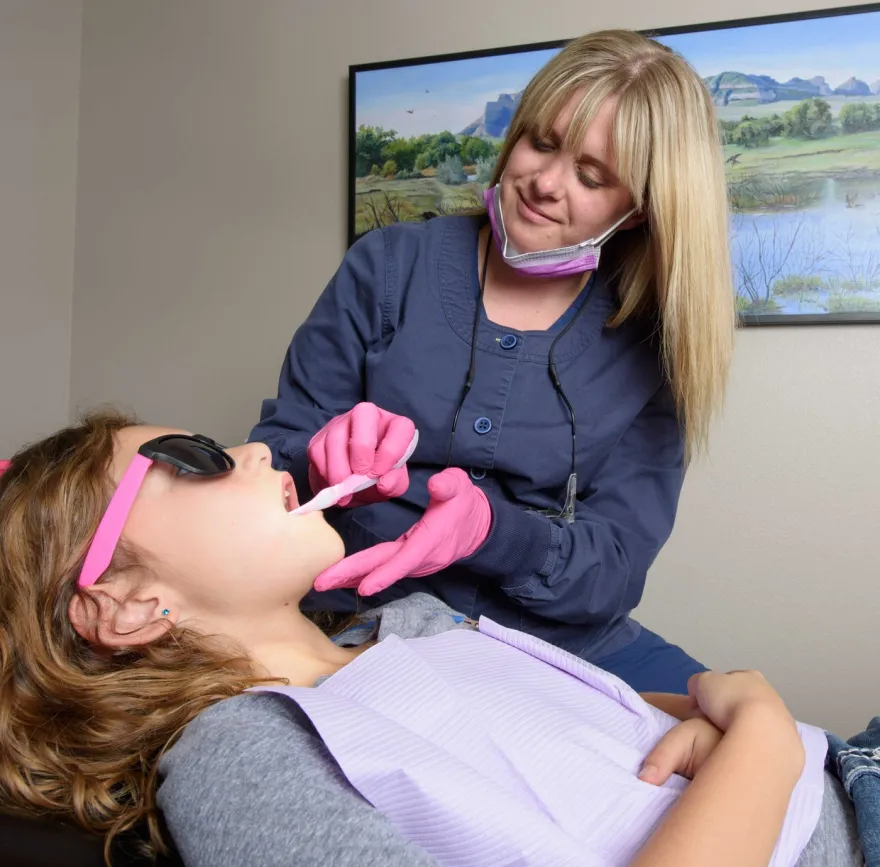 A hygienist treating a reclined patient who is wearing protective glasses.
