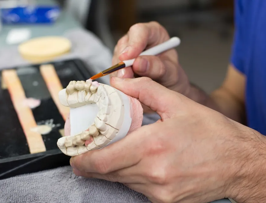 A technician shaping a dental model on the bench.
