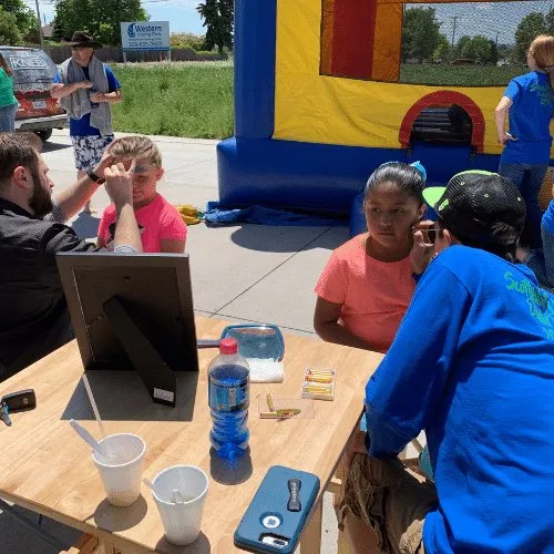 Volunteers running an activity table outdoors with a bouncy castle behind them.