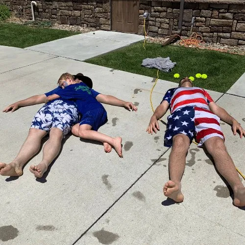 Two children lying on the pavement, soaked, after a turn at the dunk tank.