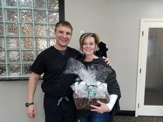 Two staff members indoors holding a wrapped gift basket.