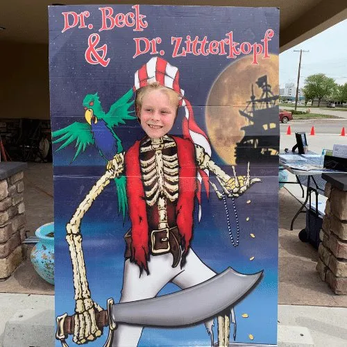 A child posing behind a painted pirate photo board lettered "Dr. Beck & Dr. Zitterkopf".