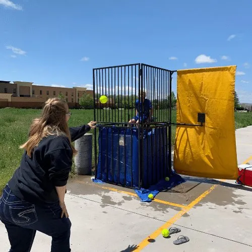 A woman throwing a ball at a dunk tank set up on grass.