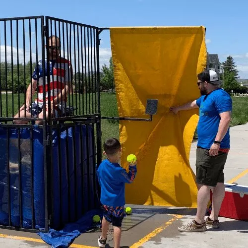 A child at the dunk-tank target while a volunteer resets it.