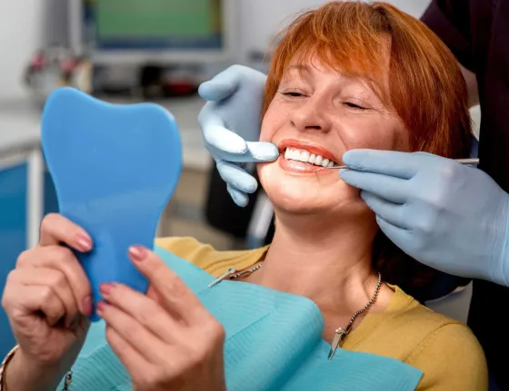 A patient holding a hand mirror while a clinician fits a restoration.