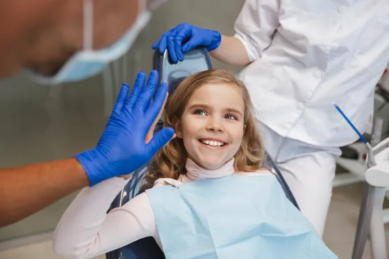 A child in the dental chair gives her dentist a high five while an assistant looks on.