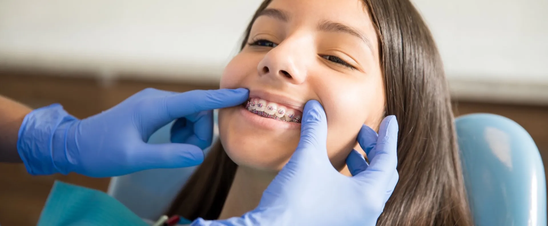 A young patient in braces having her teeth checked by gloved hands.